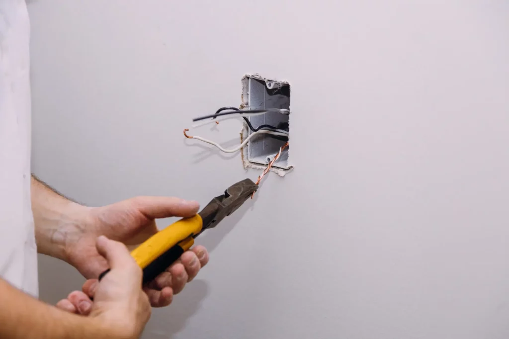 Electrician stripping wires at a wall box before installing a grounded outlet